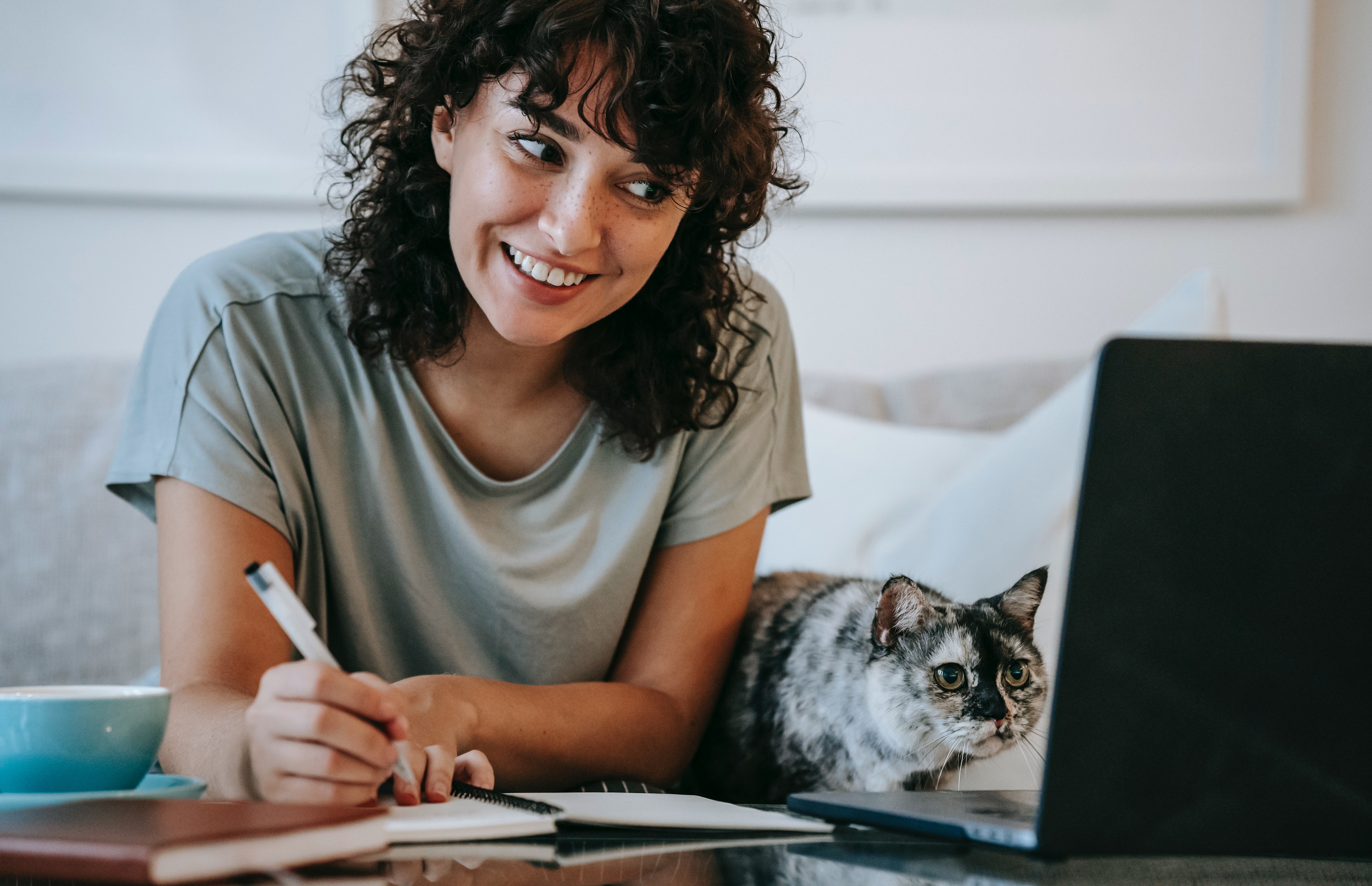 Woman with cat writing in planner while using laptop to search pet business insurance